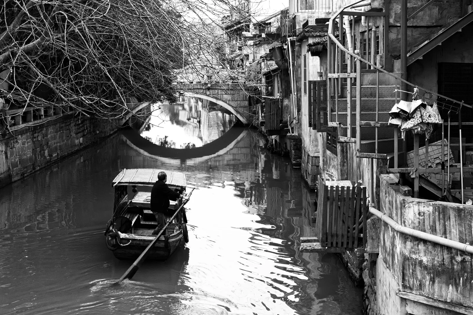 Black-and-white view of a boat and stone bridge on a canal in Suzhou