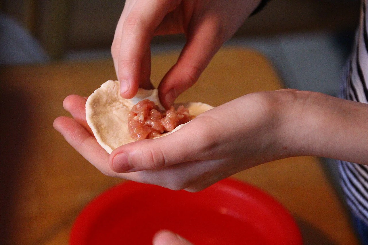 Hands preparing a filled dough parcel